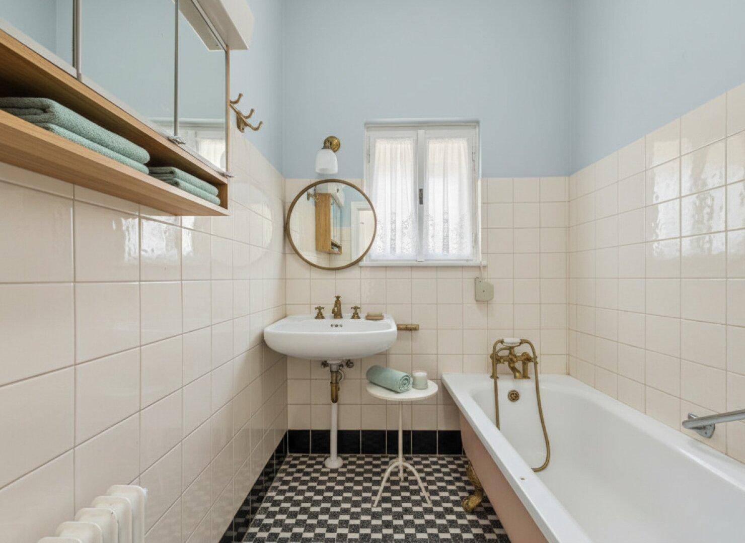 Badezimmer mit kariertem Fliesenboden, Badewanne und Waschbecken.