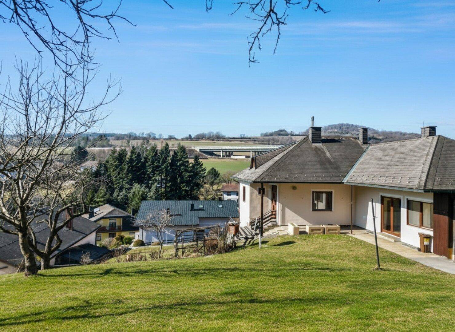 Haus in Hanglage mit weitem Blick über die grüne Landschaft und eine Autobahnbrücke.