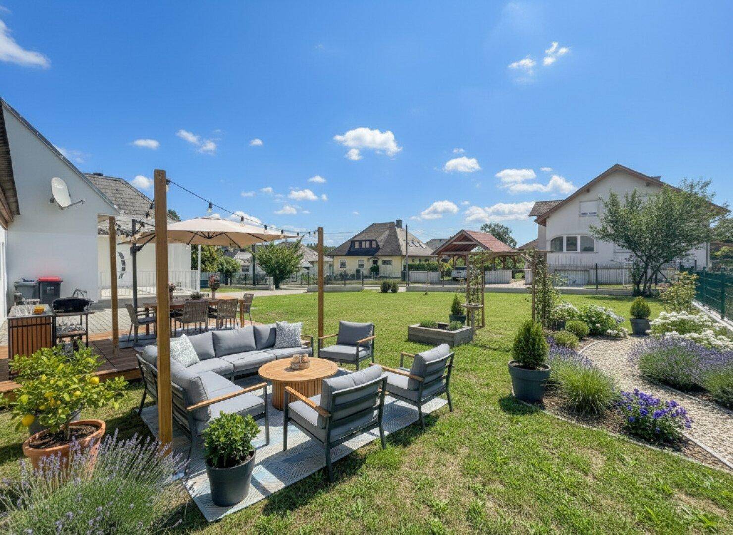 Gemütlicher Außenbereich mit Sitzgelegenheiten, Rasenfläche und mediterranen Pflanzen im Garten.