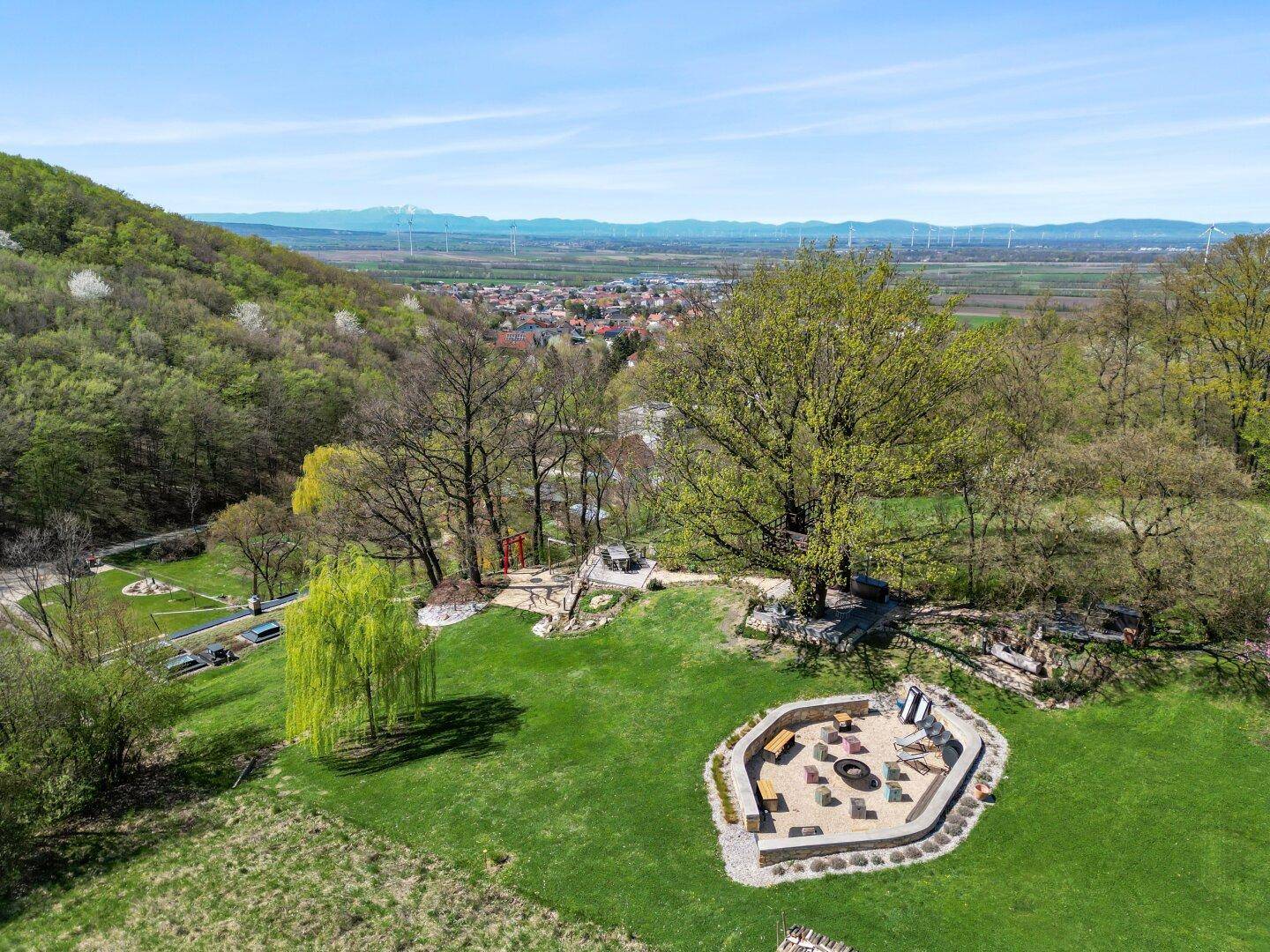 Weitläufiger Gartenbereich mit Feuerstelle, Spielplatz und Blick auf die Landschaft.