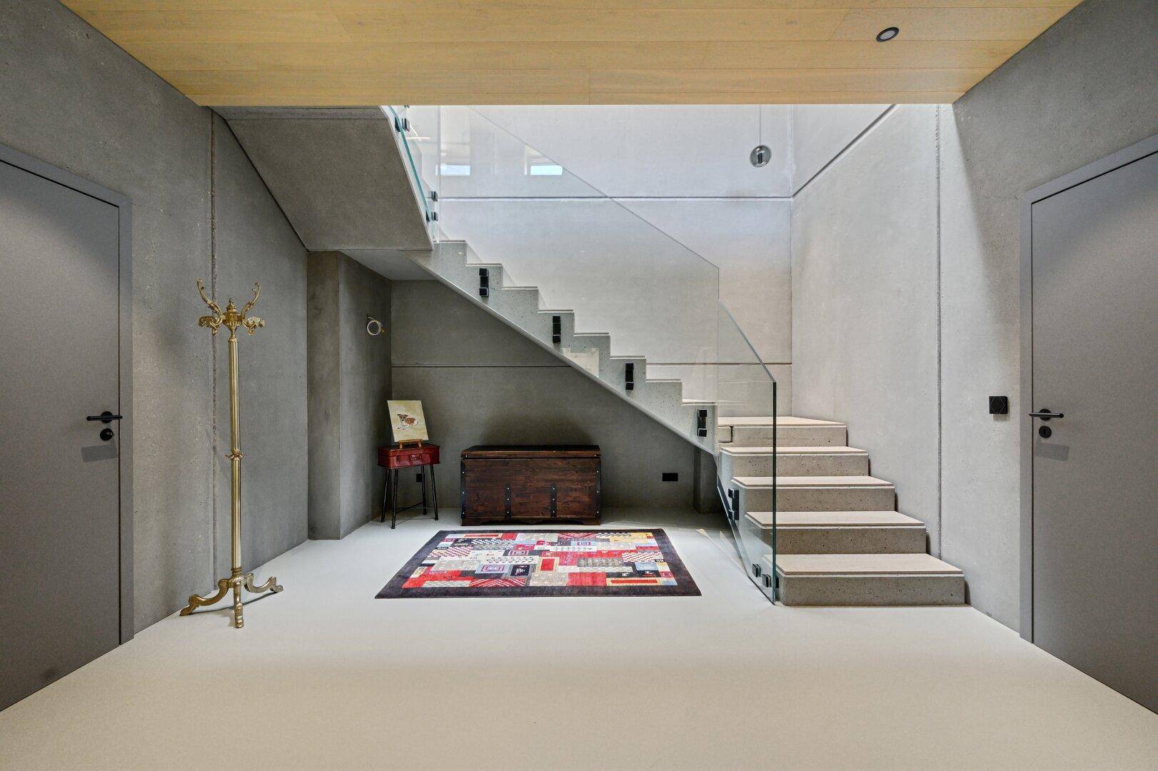 Moderner Eingangsbereich mit Betonelementen, Holzdecke und eleganter Glastreppe.