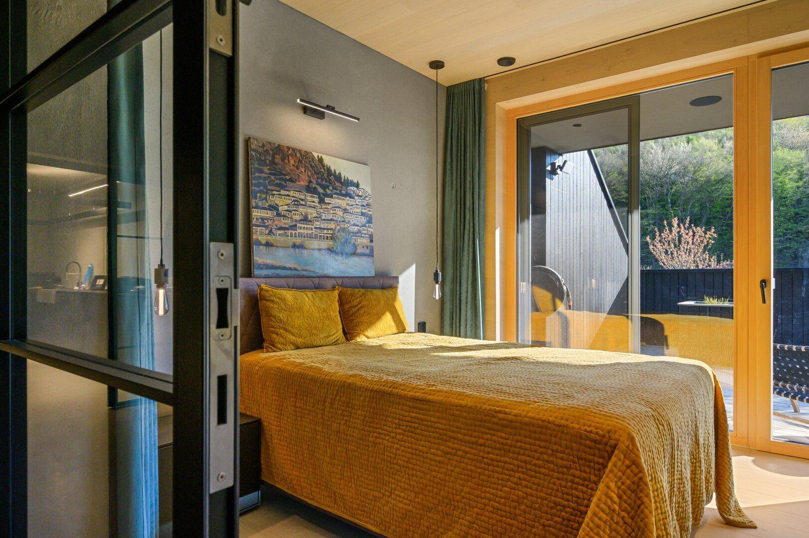 Helles Schlafzimmer mit Holzboden, gelber Bettwäsche und Zugang zur Terrasse.
