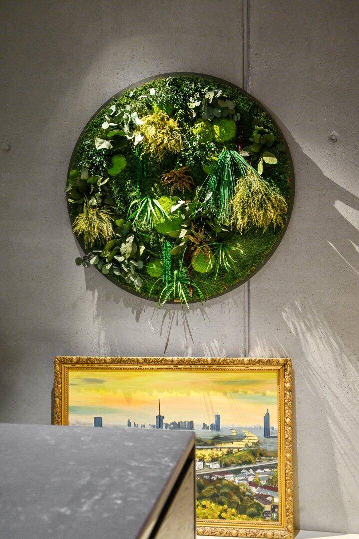 Dekoratives Moosbild an der Wand über einem gerahmten Stadtbild.