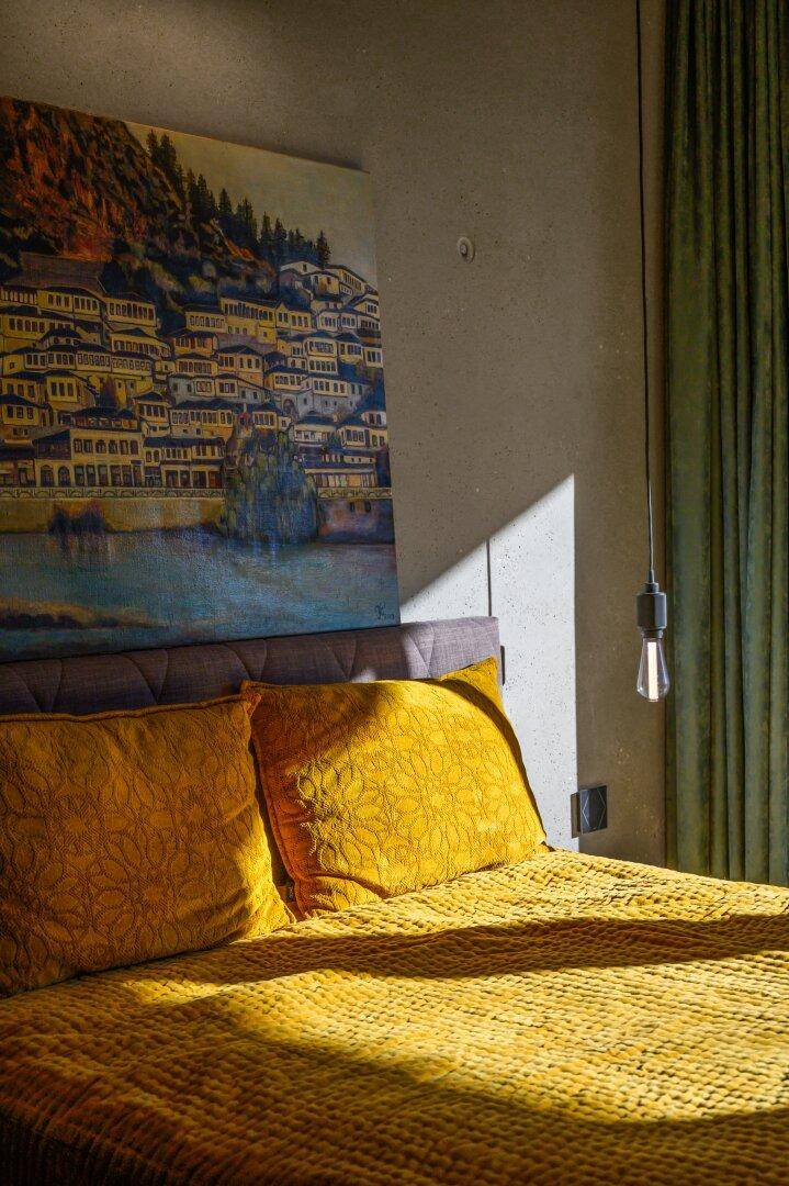 Detailansicht des Bettes mit gelber Bettwäsche und Kunstwerk an der Wand.