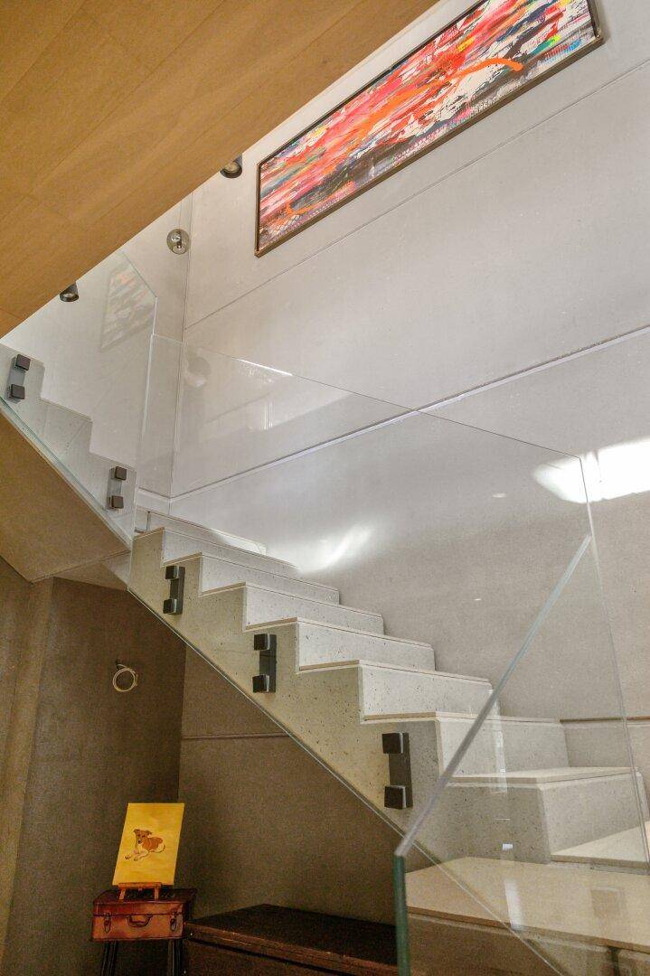 Moderne Treppe mit Glasgeländer und Kunstwerk an der Wand, lichtdurchflutet.