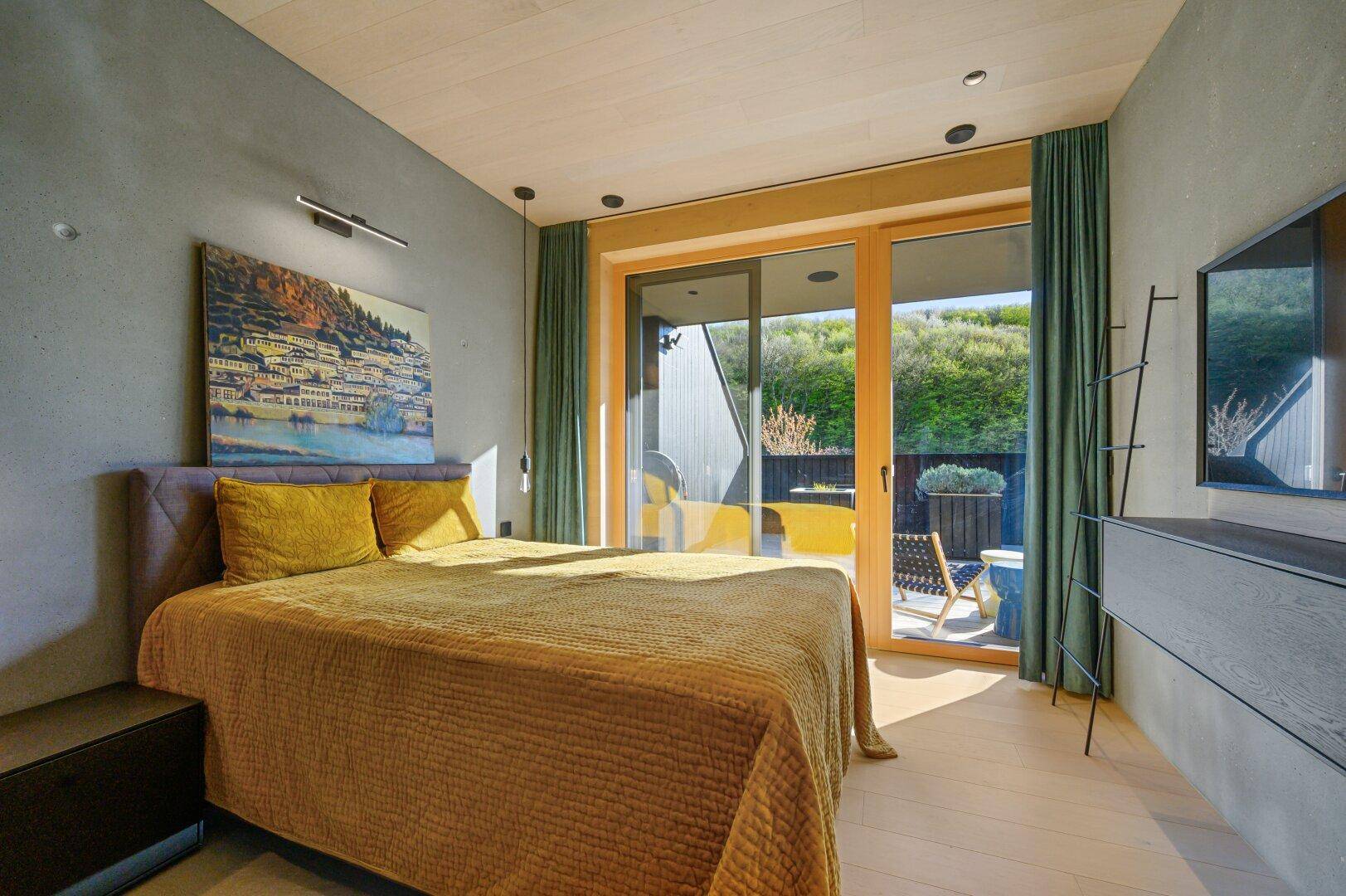Geräumiges Schlafzimmer mit Holzboden, großen Fenstern und Blick ins Grüne.