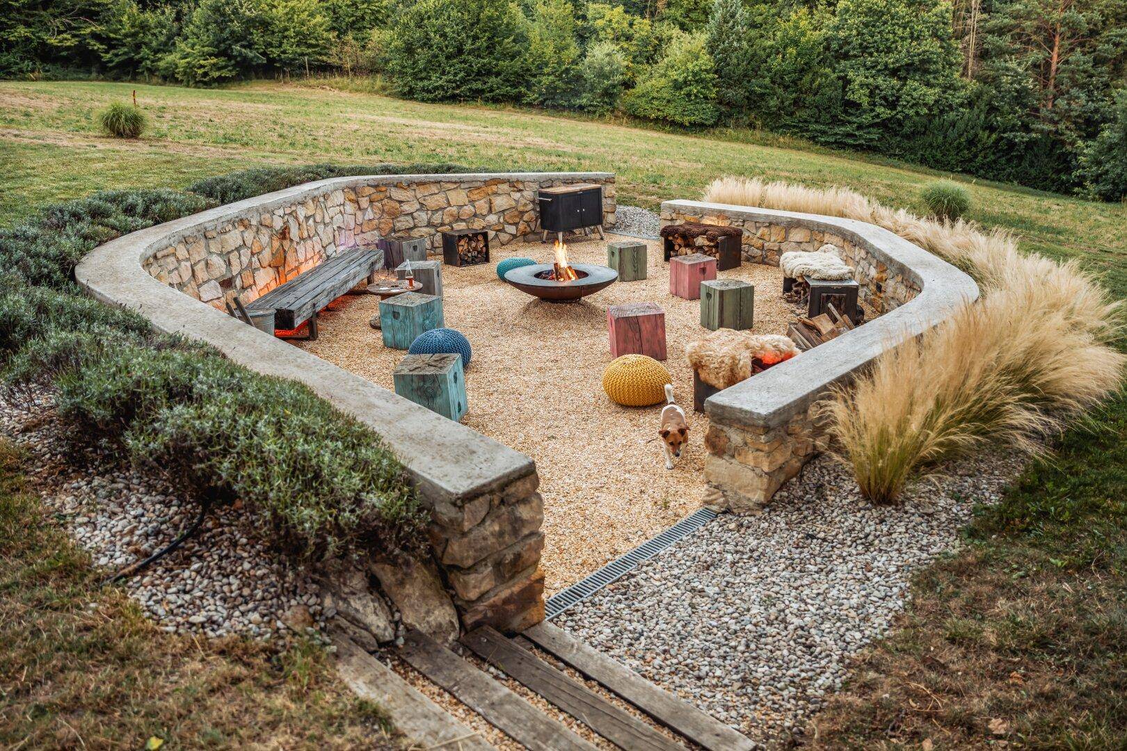 Runde Feuerstelle im Garten, umgeben von einer Steinmauer und Pflanzen.