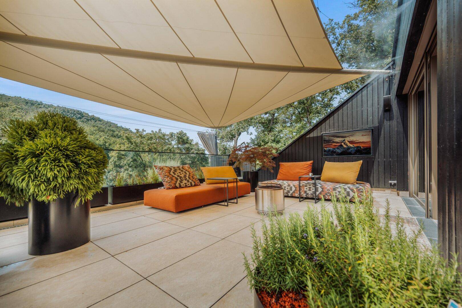 Sonnige Terrasse mit Lounge-Möbeln, Sonnensegel und Panoramablick.
