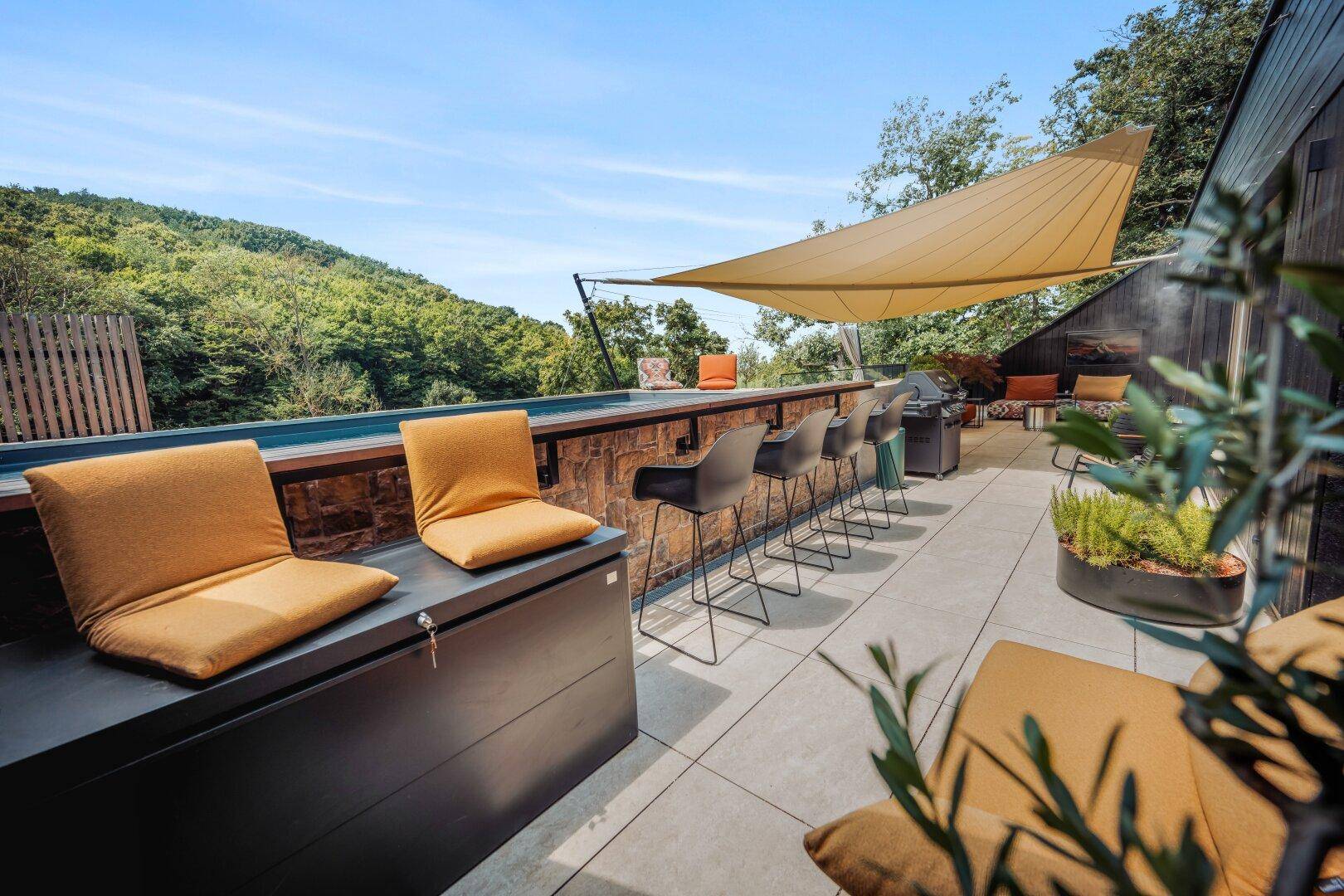 Terrasse mit Außenbar, Barhockern und Grillbereich, umgeben von Natur.