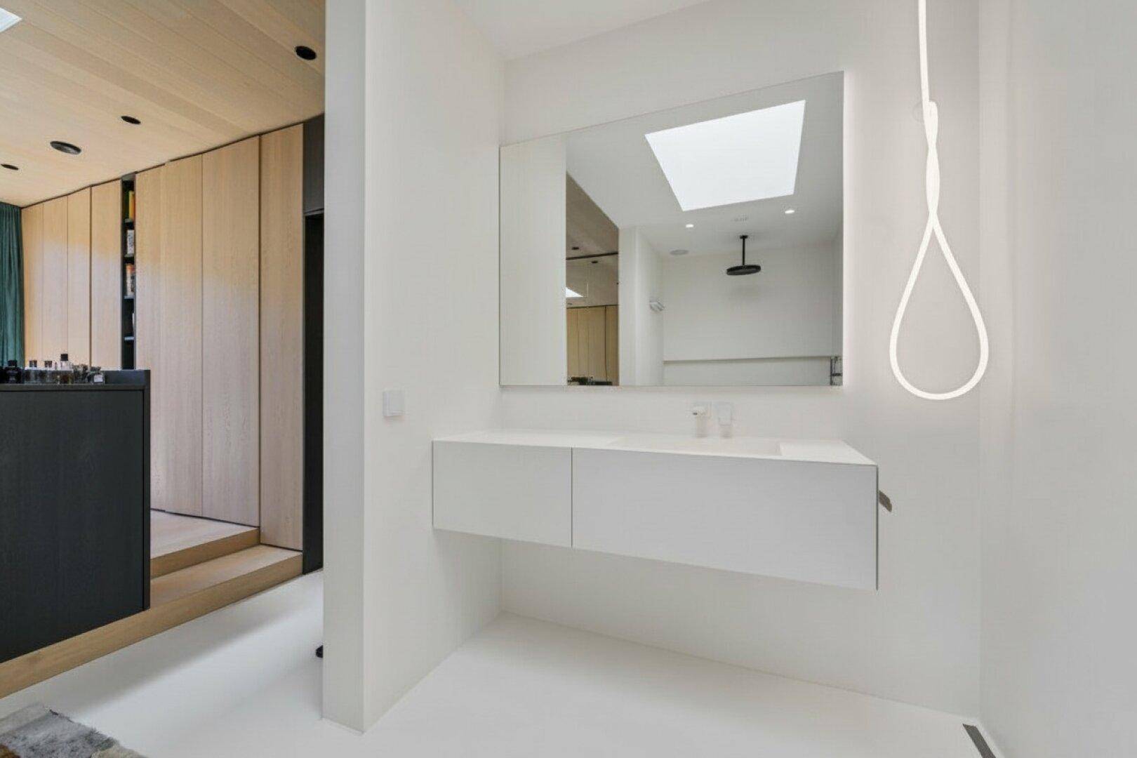Modernes Badezimmer mit schwebendem Waschtisch, großem Spiegel und Oberlicht.