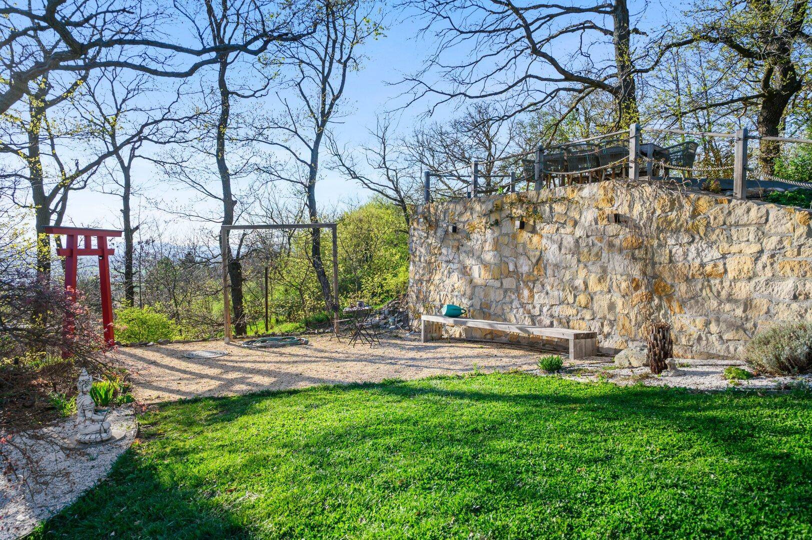 Gartenbereich mit Steinmauer, Sitzbank und Blick auf die grüne Umgebung.