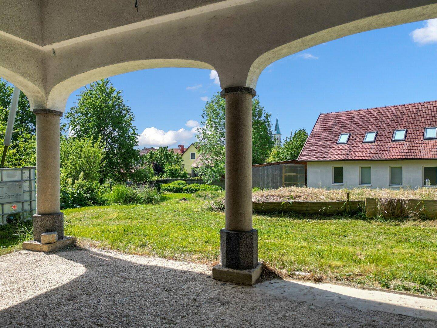 Überdachte Terrasse mit Säulen und Blick auf den Garten.