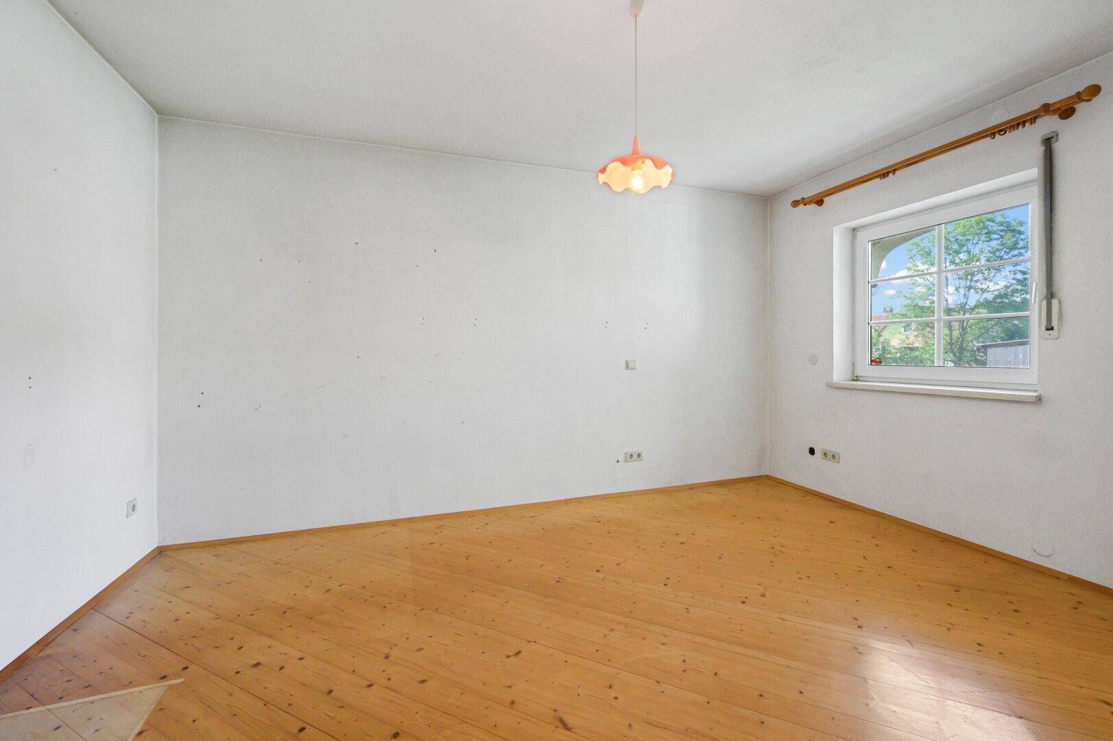 Leeres Zimmer mit Holzboden und Fenster, ideal als Schlaf- oder Arbeitszimmer.