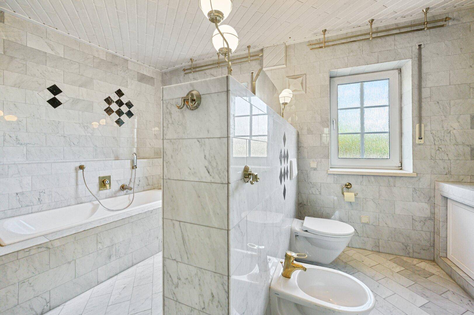 Elegantes Marmorbad mit Bidet, Toilette, Waschbecken und Fenster.