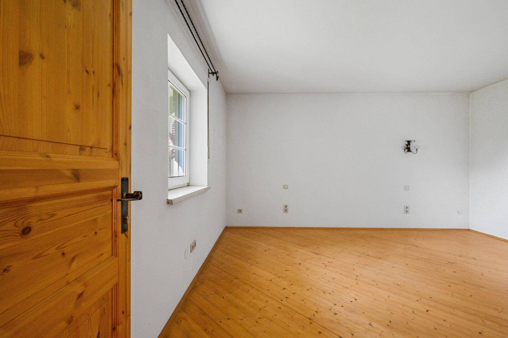 Leeres Schlafzimmer mit Holzboden und Holztür.