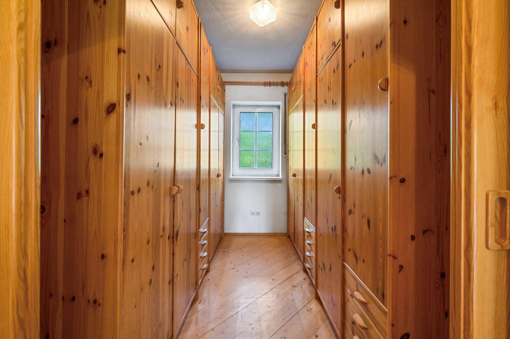 Begehbarer Kleiderschrank mit Holzschränken und Fenster.