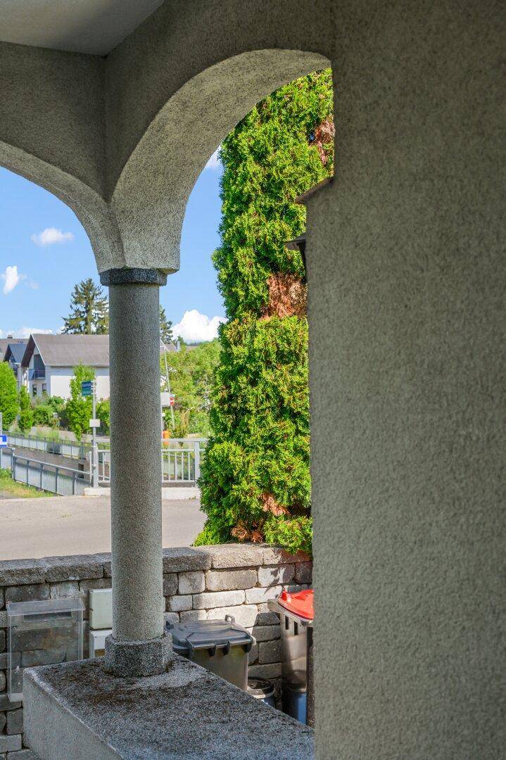 Blick durch einen Torbogen auf die Straße und die grüne Umgebung.