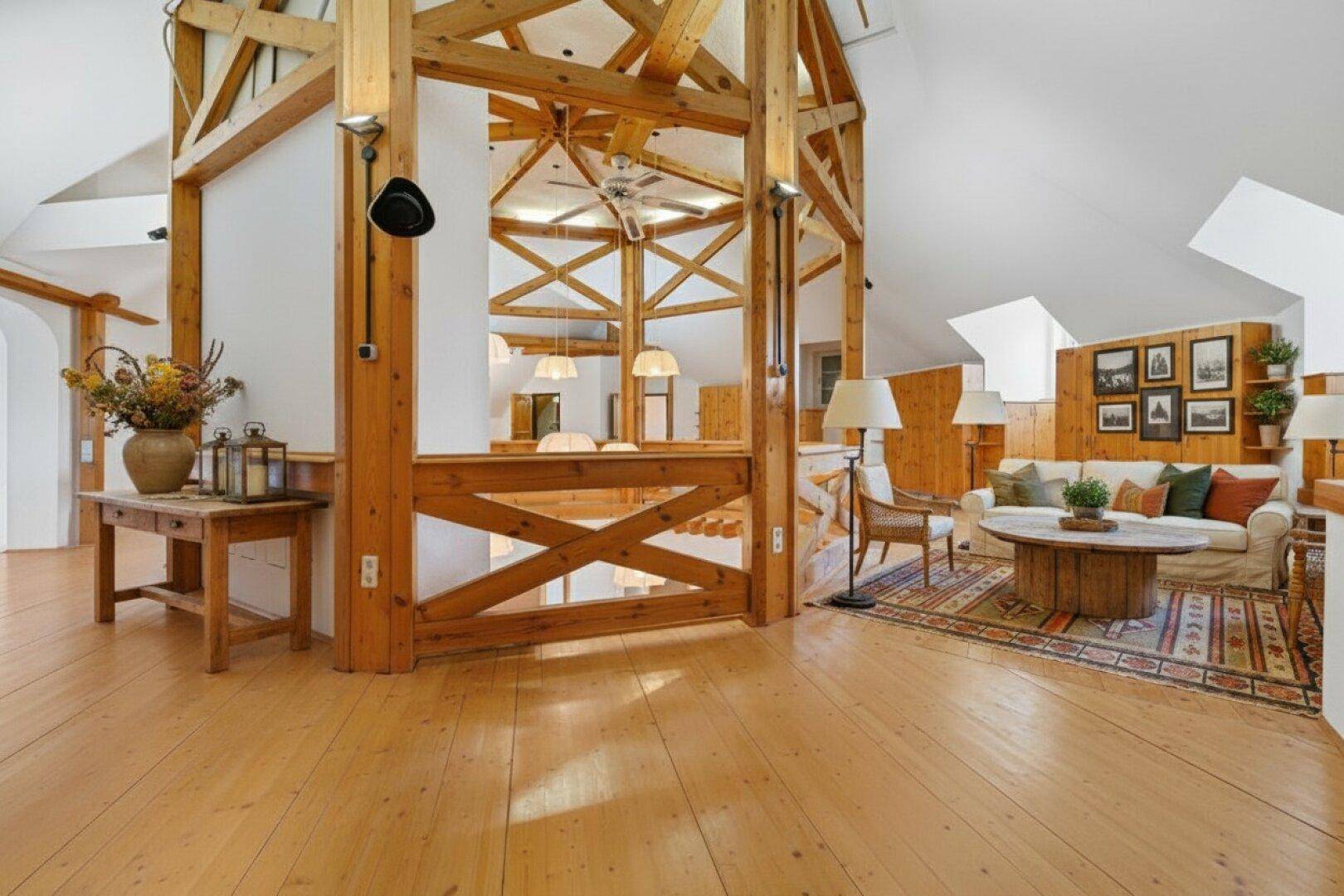 Geräumiger Wohnbereich mit sichtbaren Holzträgern, Holzboden und gemütlicher Sitzecke.