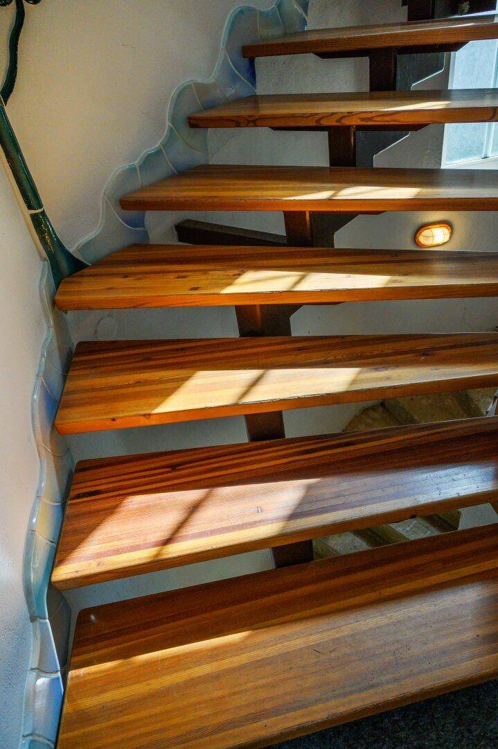 Helle Holztreppe mit dekorativem, wellenförmigem Wandelement und natürlichem Lichteinfall.