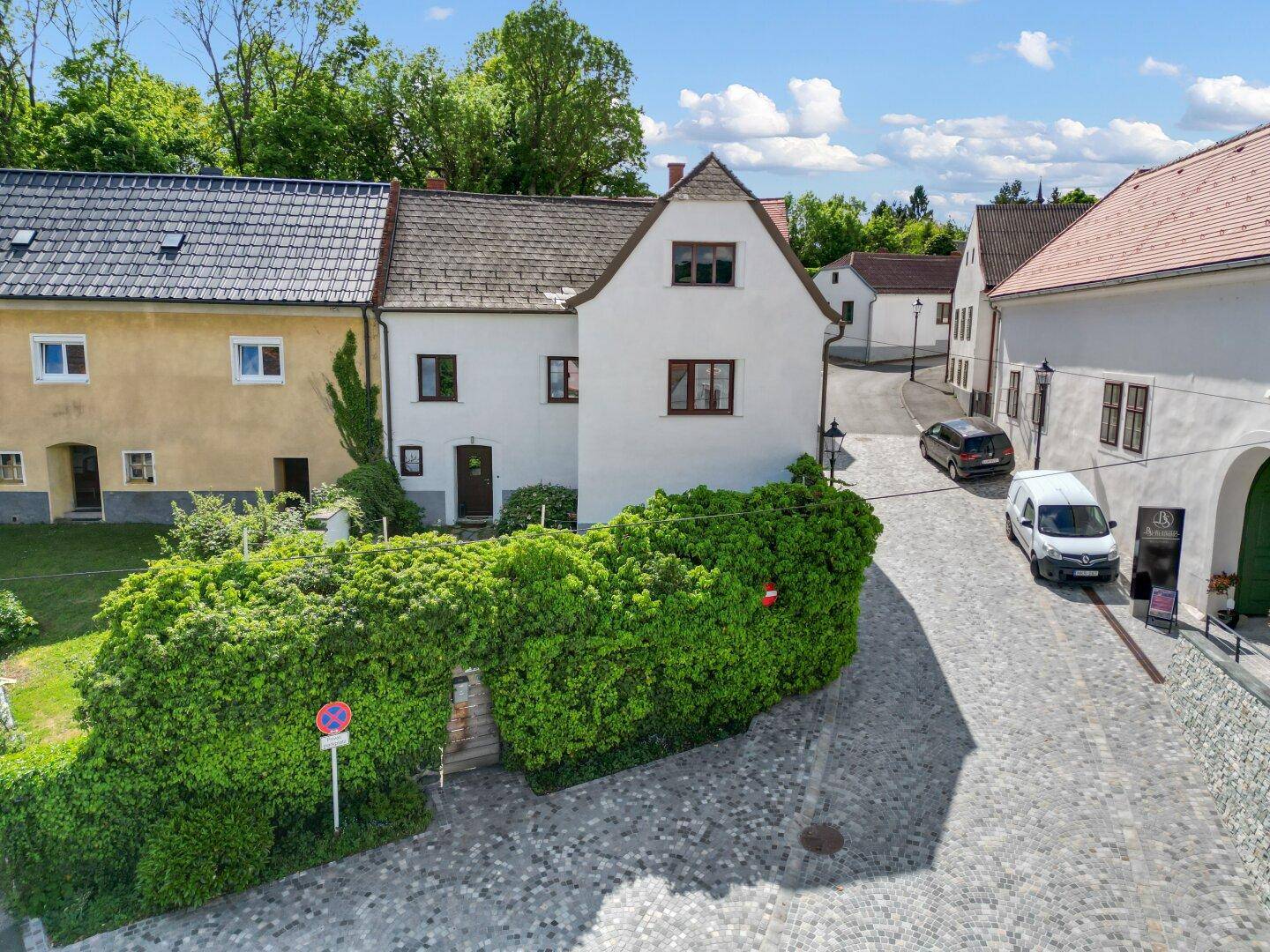Historisches Gebäude mit begrüntem Eingangsbereich an einer gepflasterten Gasse in ländlicher Umgebung.