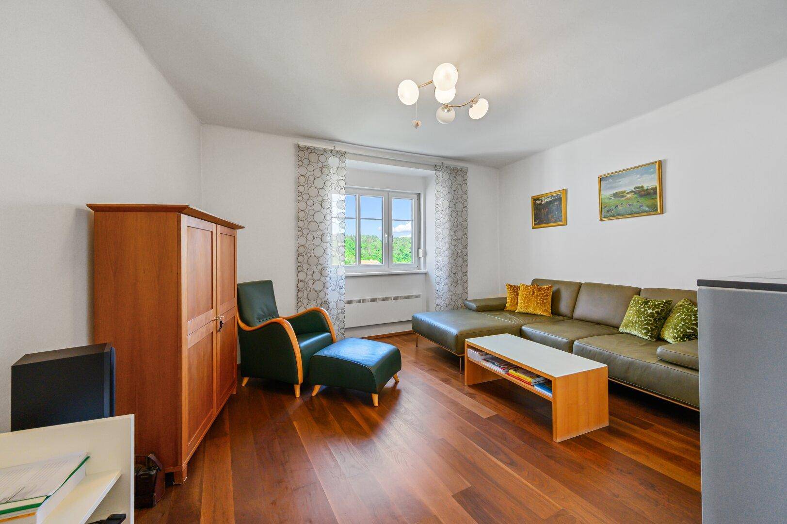 Gemütliches Wohnzimmer mit Holzboden, bequemer Couch und Blick ins Grüne.