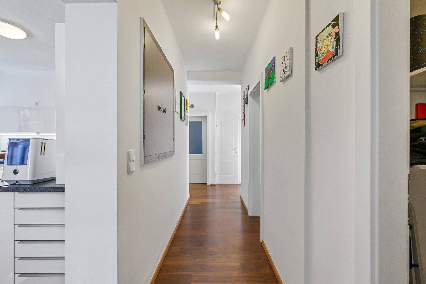 Langer Flur mit Holzboden, weißen Wänden und Zugang zu verschiedenen Räumen.