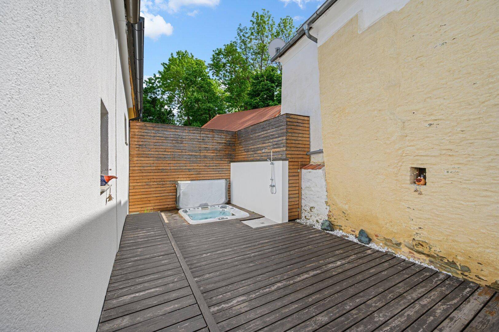 Holzterrasse mit integriertem Whirlpool und Außendusche, umgeben von Holzwänden.