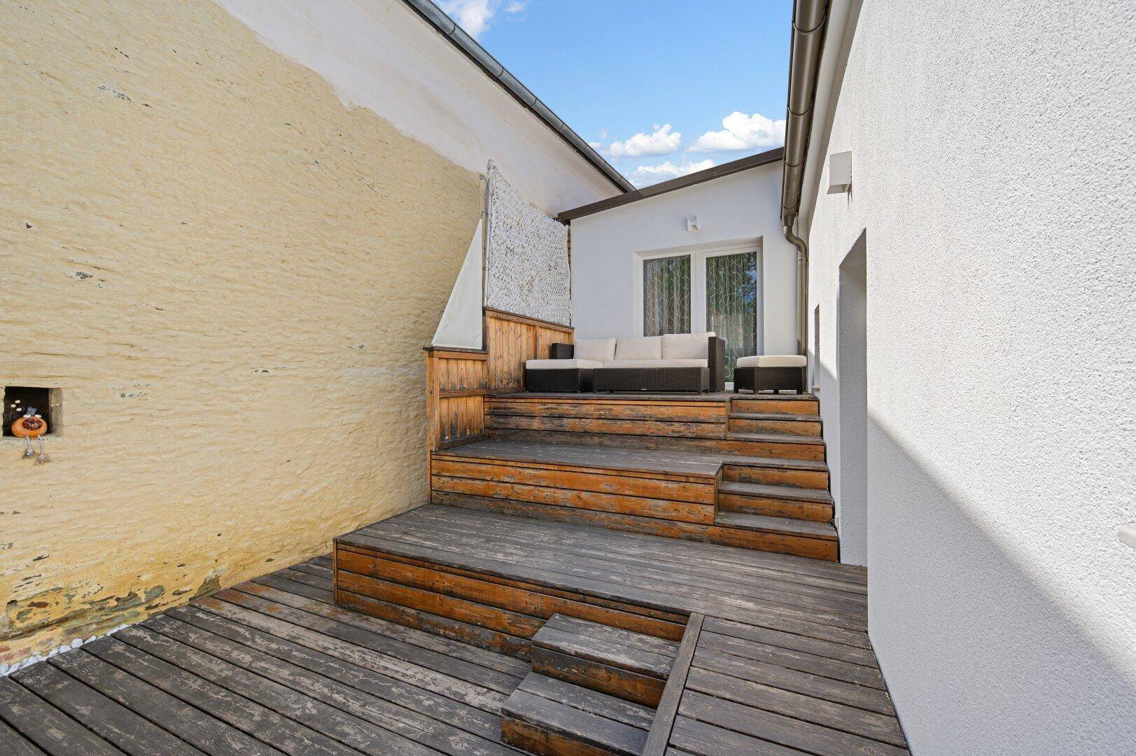 Mehrstufige Holzterrasse mit Sitzbereich und Zugang zum Innenraum des Hauses.