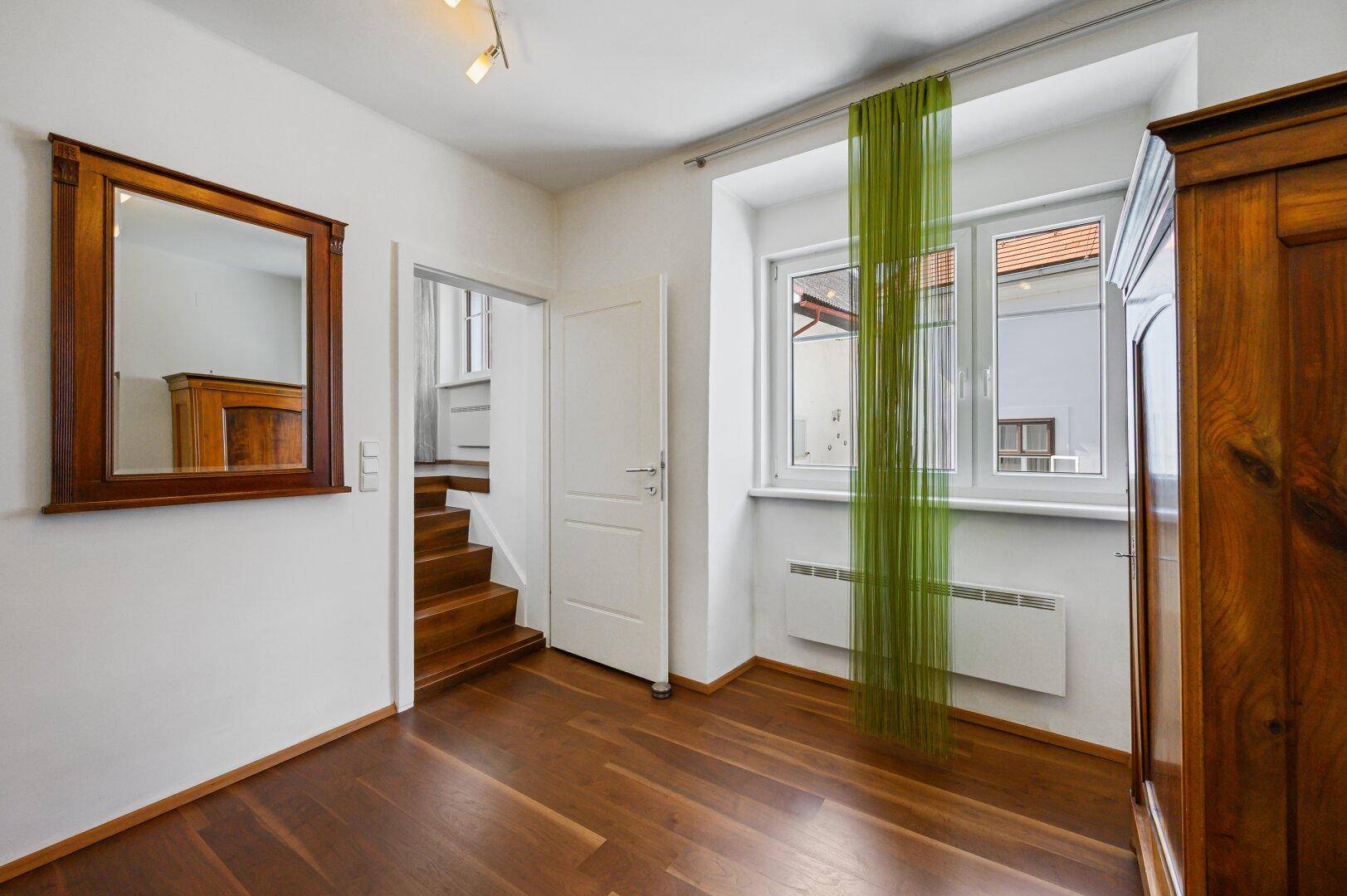 Schlafzimmer mit Holzboden, Fenster und einem großen Holzschrank.