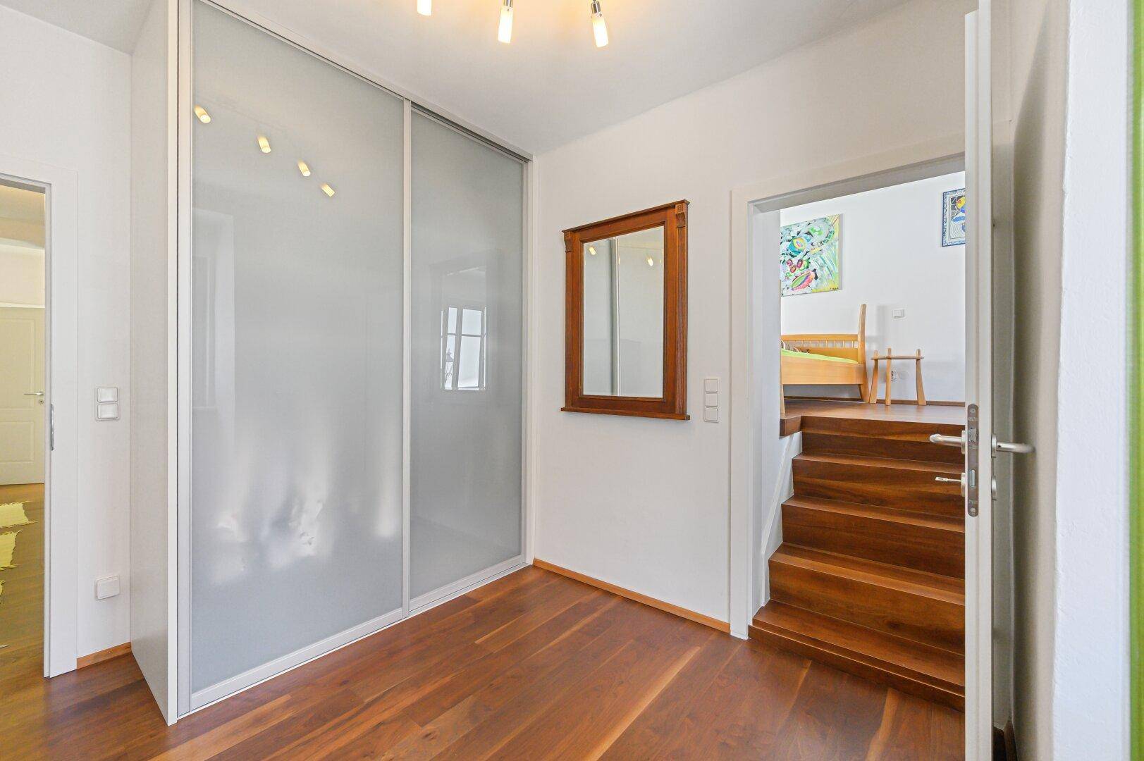Flur mit Holzboden, Spiegelschrank und Treppe zum oberen Stockwerk.