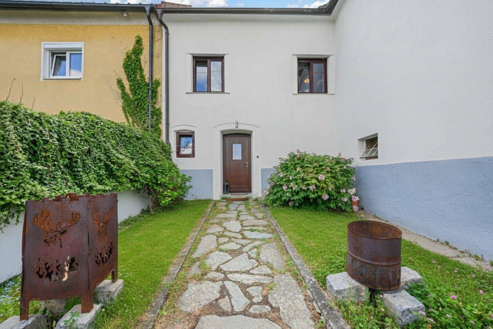Steinweg führt durch den Vorgarten mit Rasenflächen zum Eingang eines historischen Gebäudes.