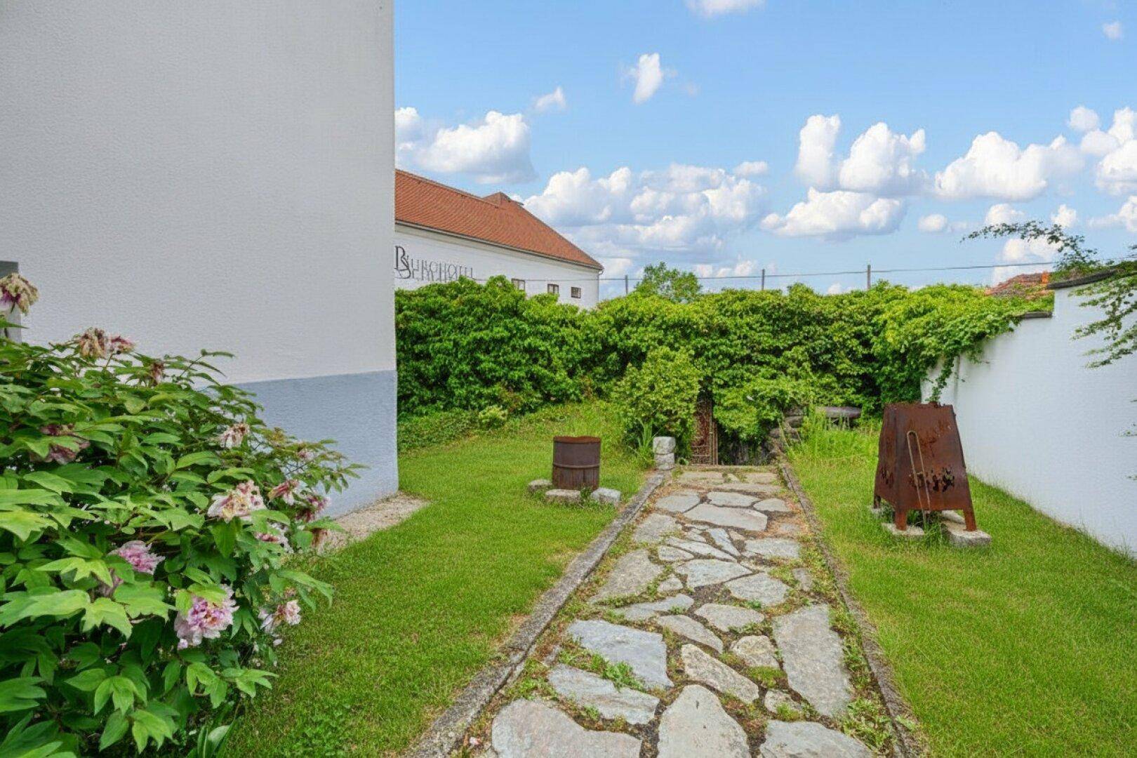 Gepflegter Gartenweg mit Rasenflächen und einer hohen Hecke, die das Grundstück begrenzt.