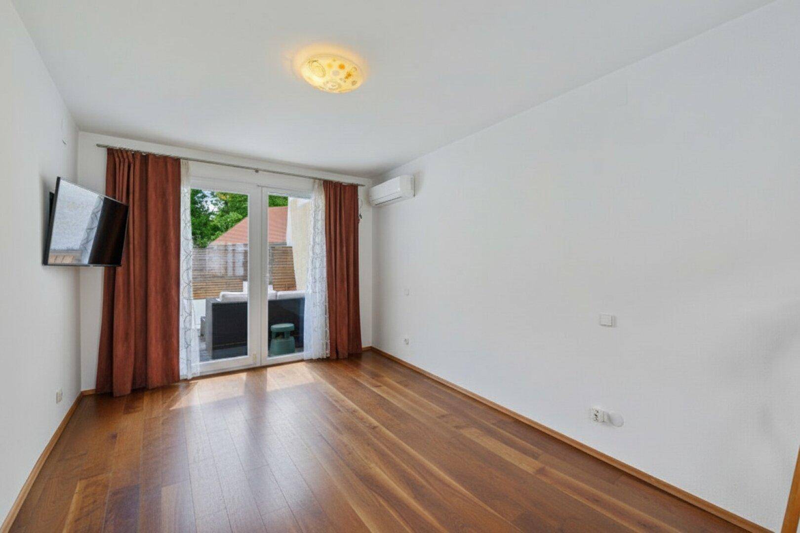 Helles Schlafzimmer mit Holzboden, Klimaanlage und Zugang zur Außenterrasse.