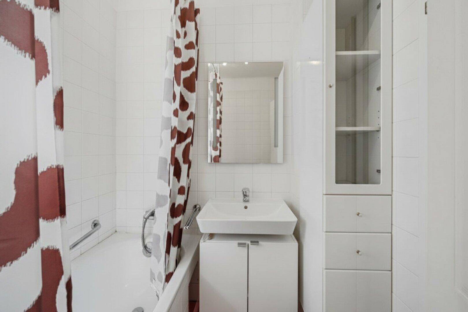 Helles Badezimmer mit Badewanne, Duschvorhang und weiß gefliesten Wänden.