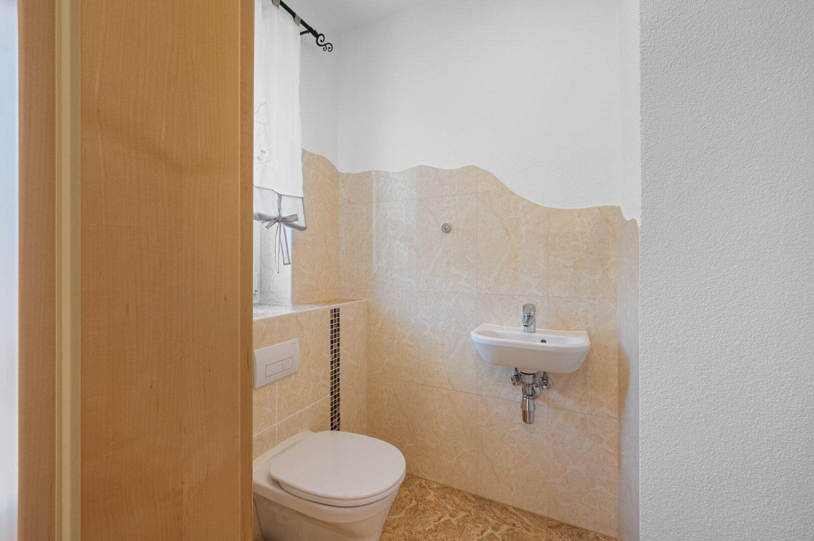 Kleines Gäste-WC mit Fenster, hellen Fliesen und wandmontierter Toilette.