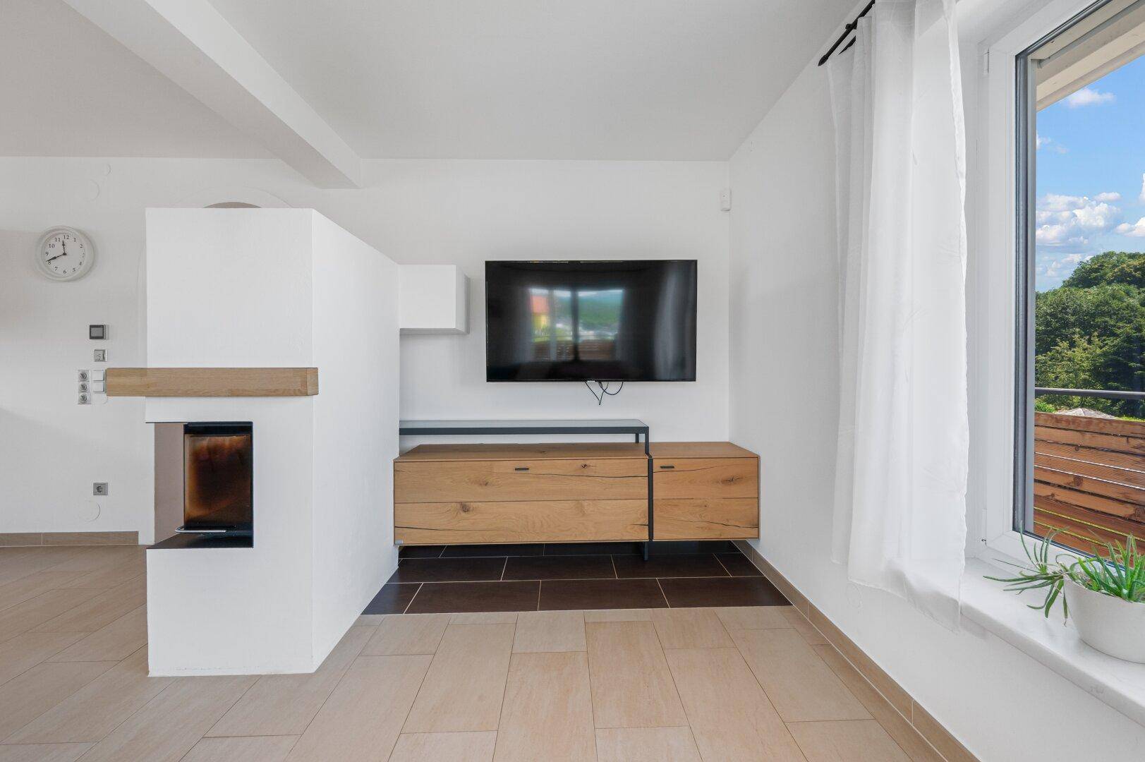 Moderner Wohnbereich mit Wandfernseher und integriertem Kamin, umgeben von hellen Wänden.