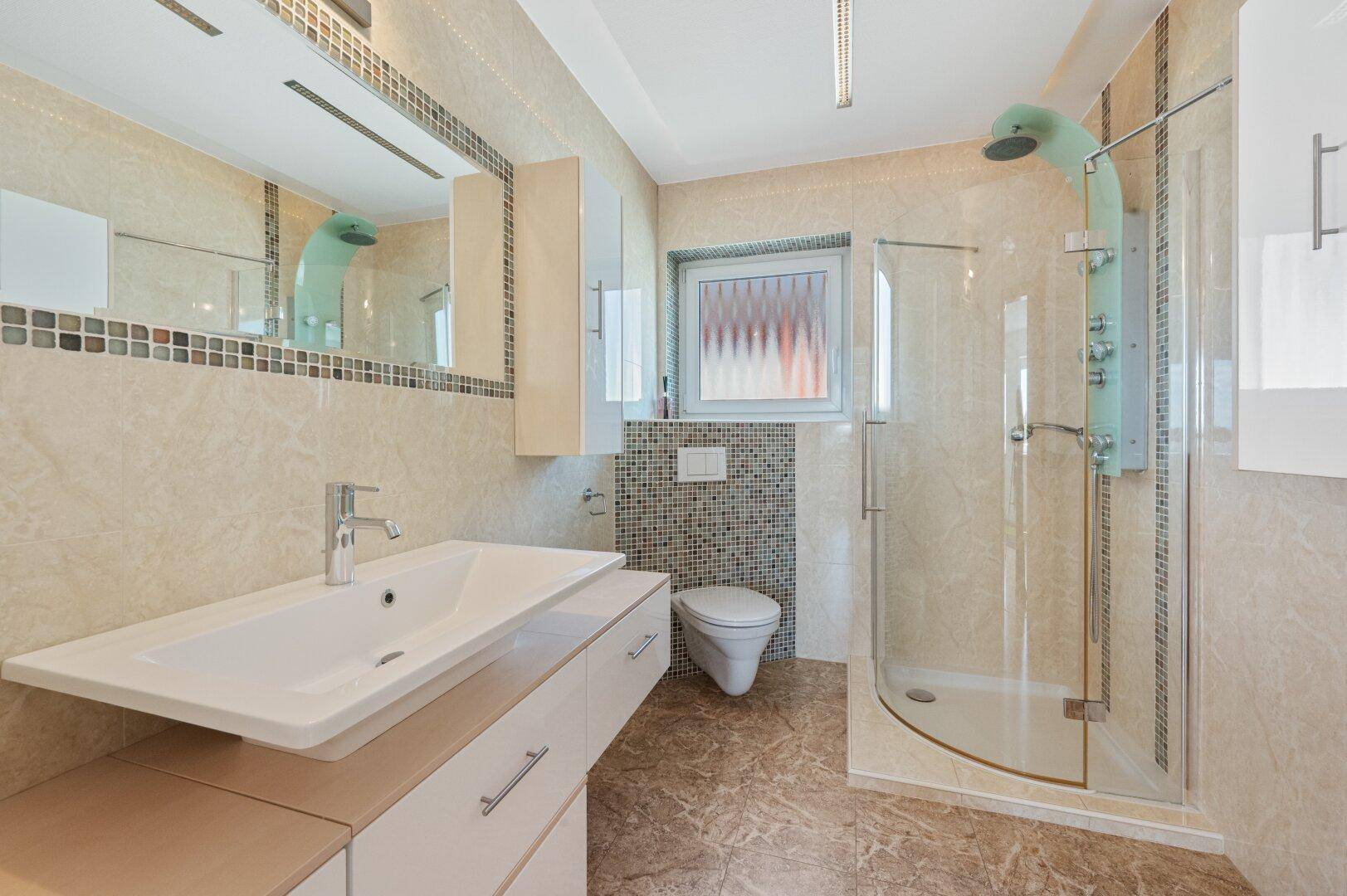 Modernes Badezimmer mit beigefarbenen Fliesen, Einzelwaschbecken, wandhängendem WC und Glasdusche.