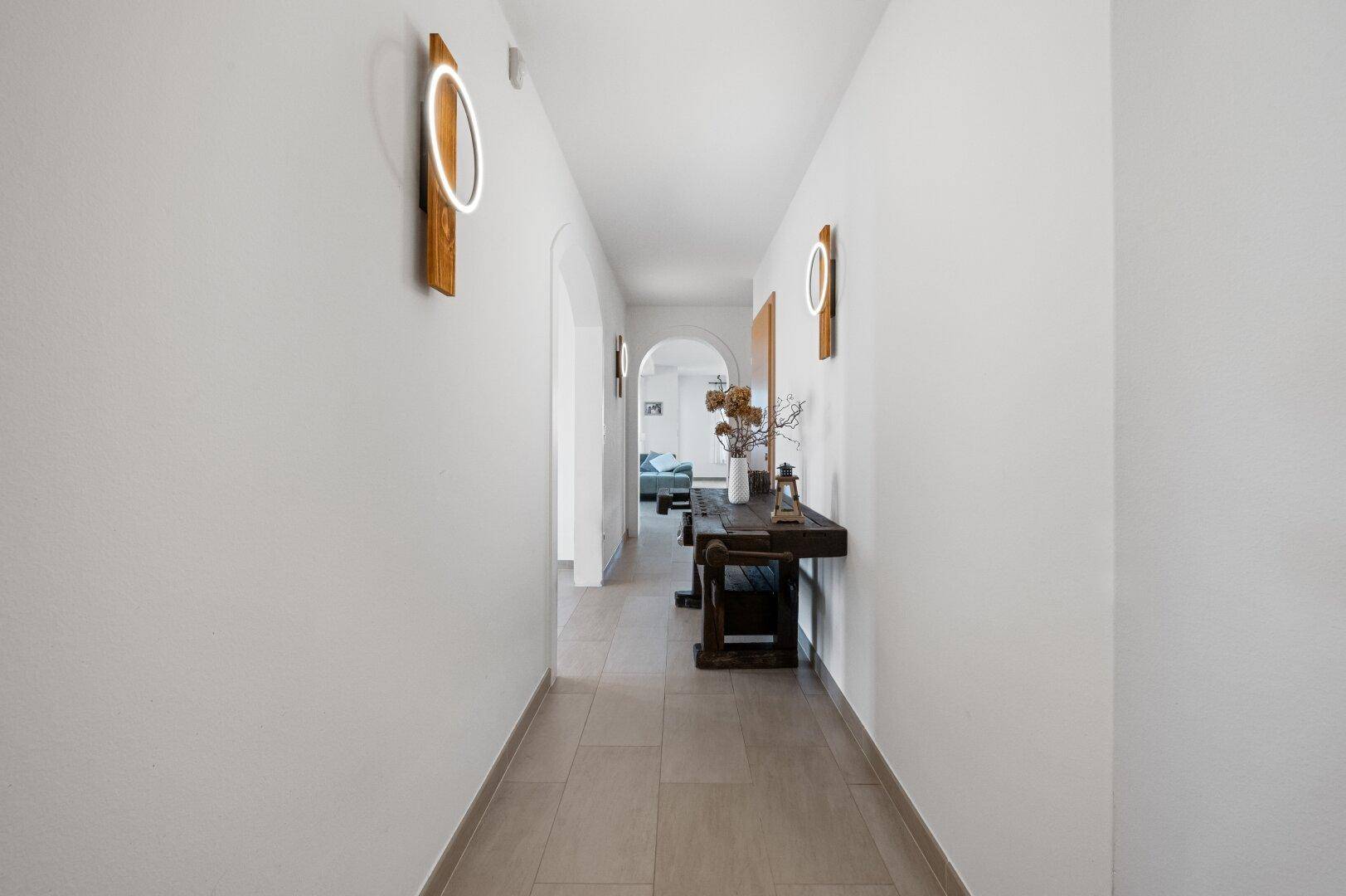 Langer, heller Flur mit modernen Wandleuchten und Blick auf weitere Räume.