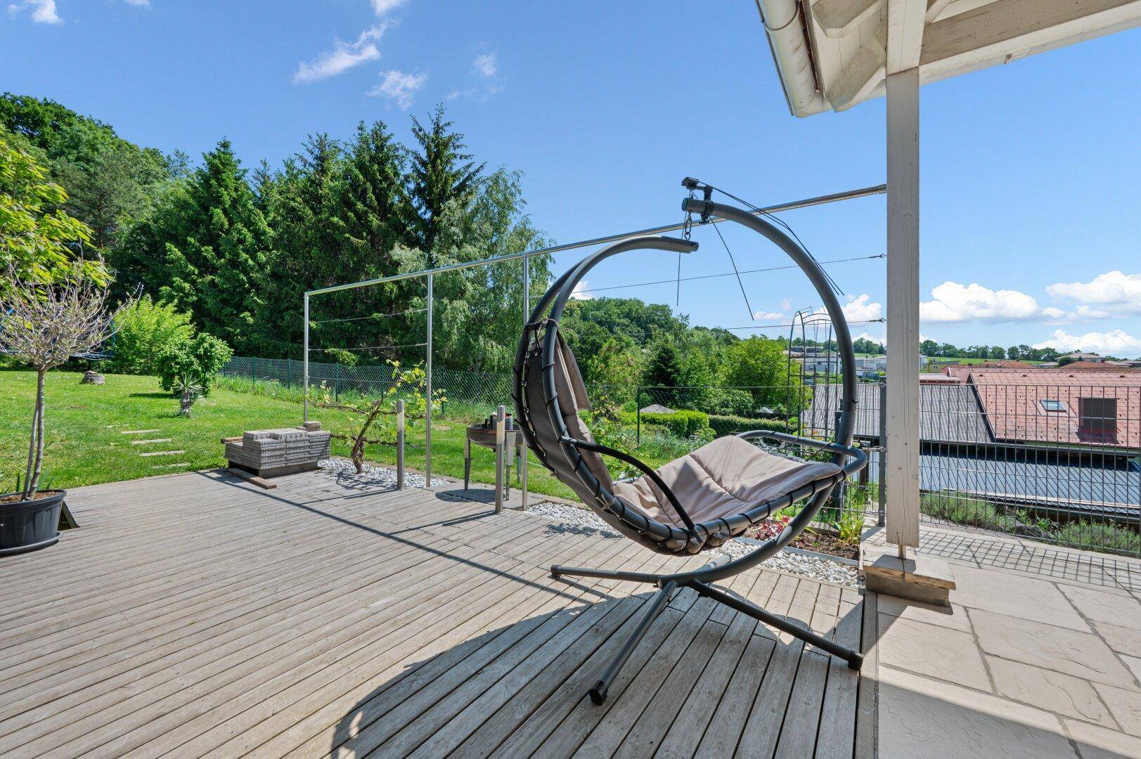 Holzterrasse mit modernem Hängesessel und weitem Blick über grüne Hügel und die umliegende Landschaft.