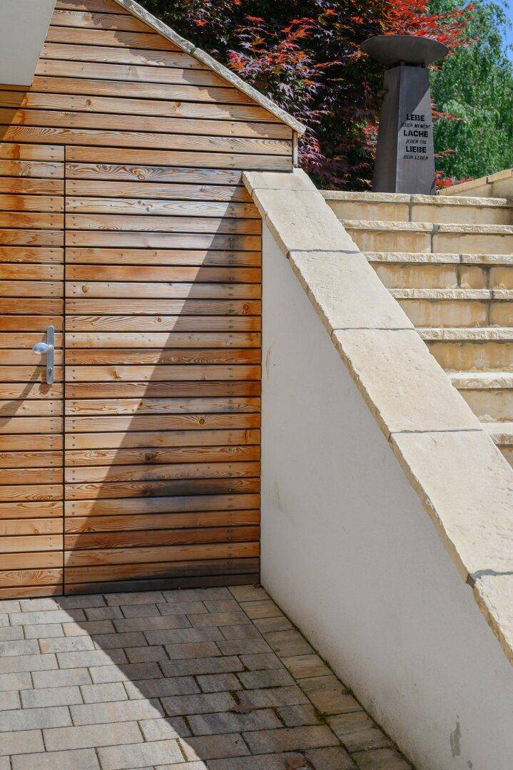 Nahaufnahme der holzverkleideten Wand und Steintreppe mit einem dekorativen Pfeiler im Hintergrund.