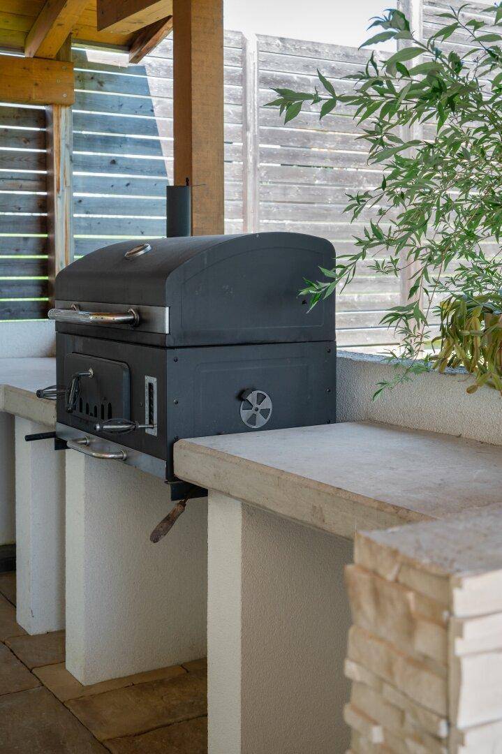 Eingebauter Grill auf einer Steinarbeitsplatte als Teil einer Außenküche mit Holzverkleidung im Hintergrund.
