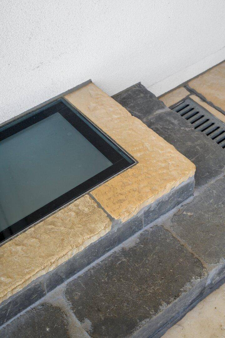 Detailansicht eines Bodenelements mit Glas und Steinplatten im Außenbereich, inklusive Entwässerungsrinne.