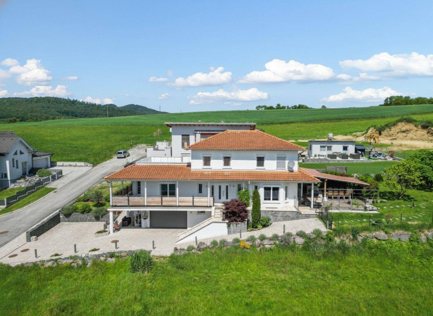Luftaufnahme des gesamten Anwesens mit Haus, Balkonen, Auffahrt und weitläufiger grüner Umgebung.
