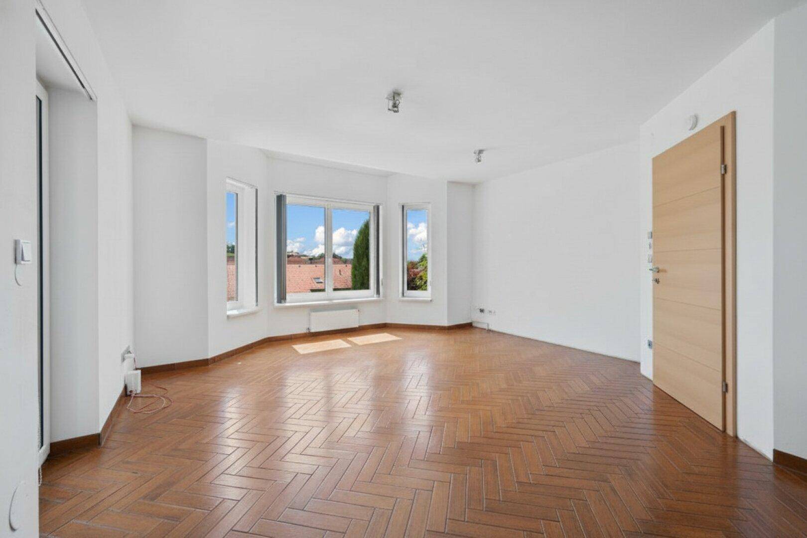 Geräumiges Zimmer mit elegantem Fischgrätparkett und großen Fenstern für viel Licht.