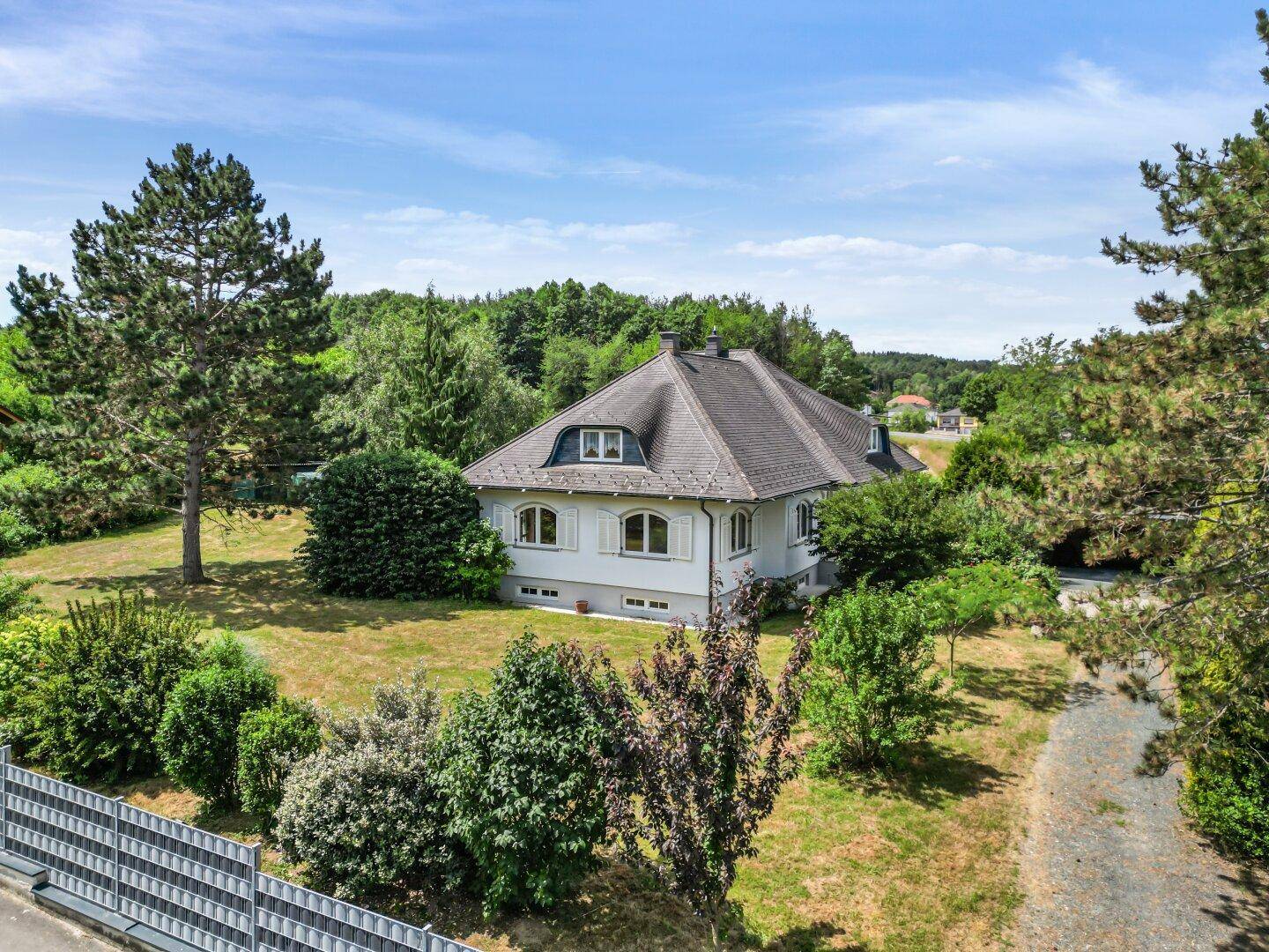 Seitenansicht des Hauses mit weitläufigem Garten, umgeben von hohen Bäumen und Natur.