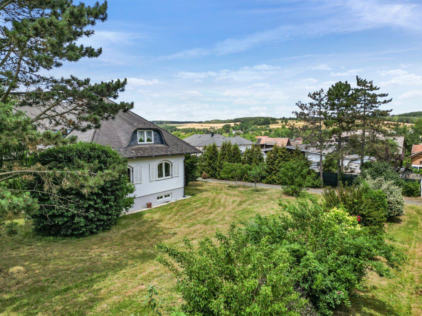 Hausansicht mit weitläufiger Rasenfläche und Blick auf die hügelige Landschaft.