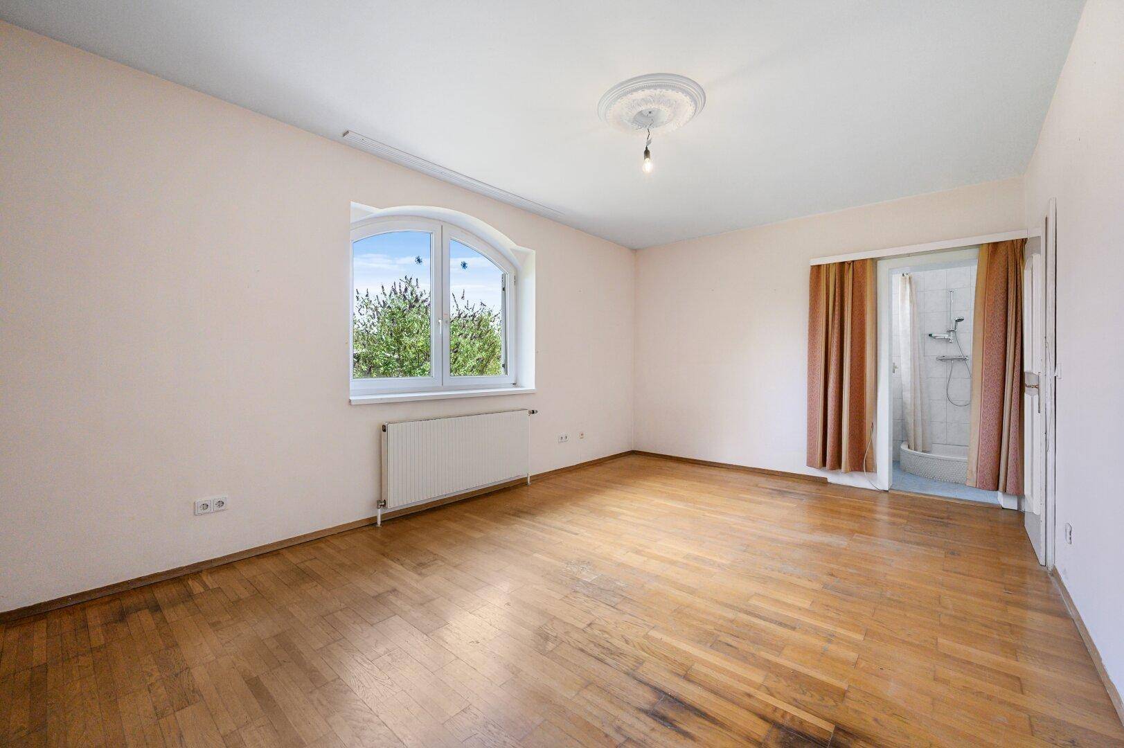 Helles Schlafzimmer mit Parkettboden, Stuckdecke und integrierter Duschkabine.