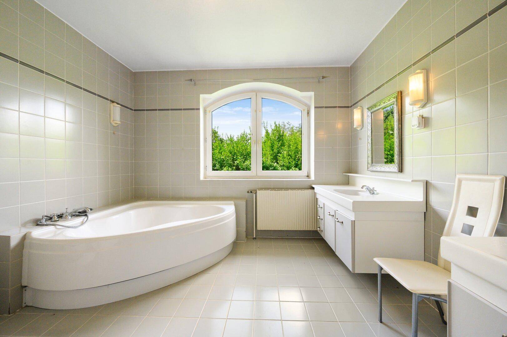 Geräumiges Badezimmer mit Eckbadewanne, großem Fenster und hellen Fliesen.
