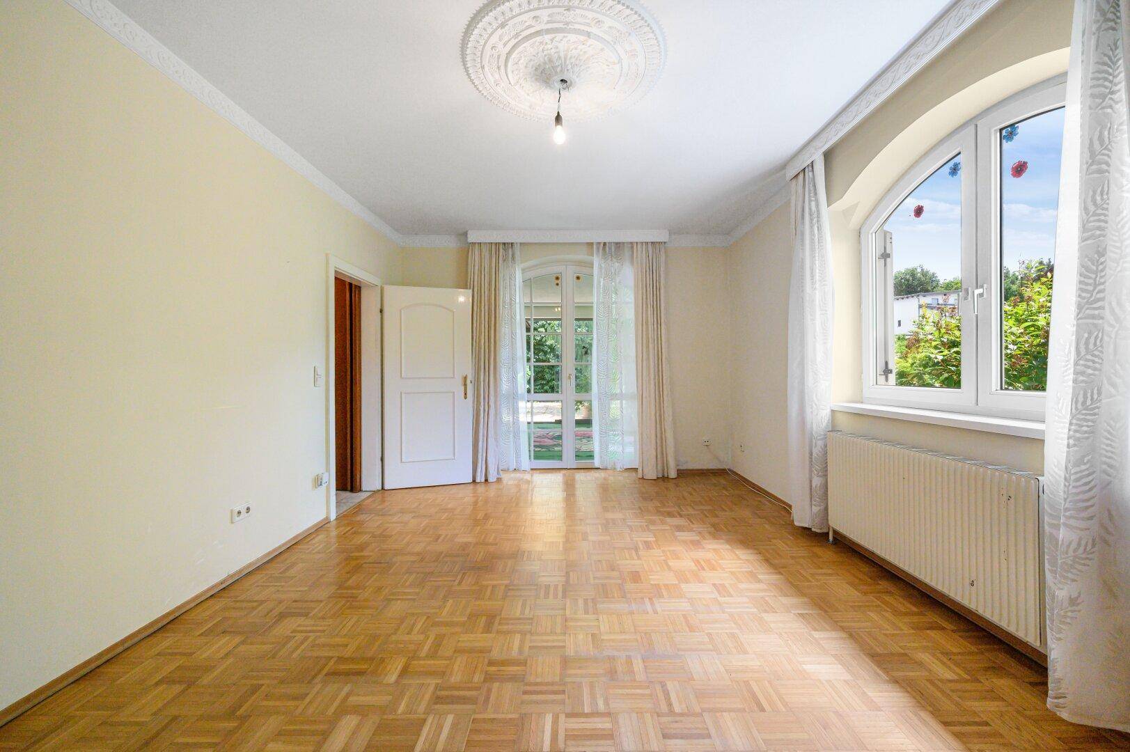 Geräumiges Schlafzimmer mit Parkettboden, Stuckdecke und Zugang zu einem Außenbereich.