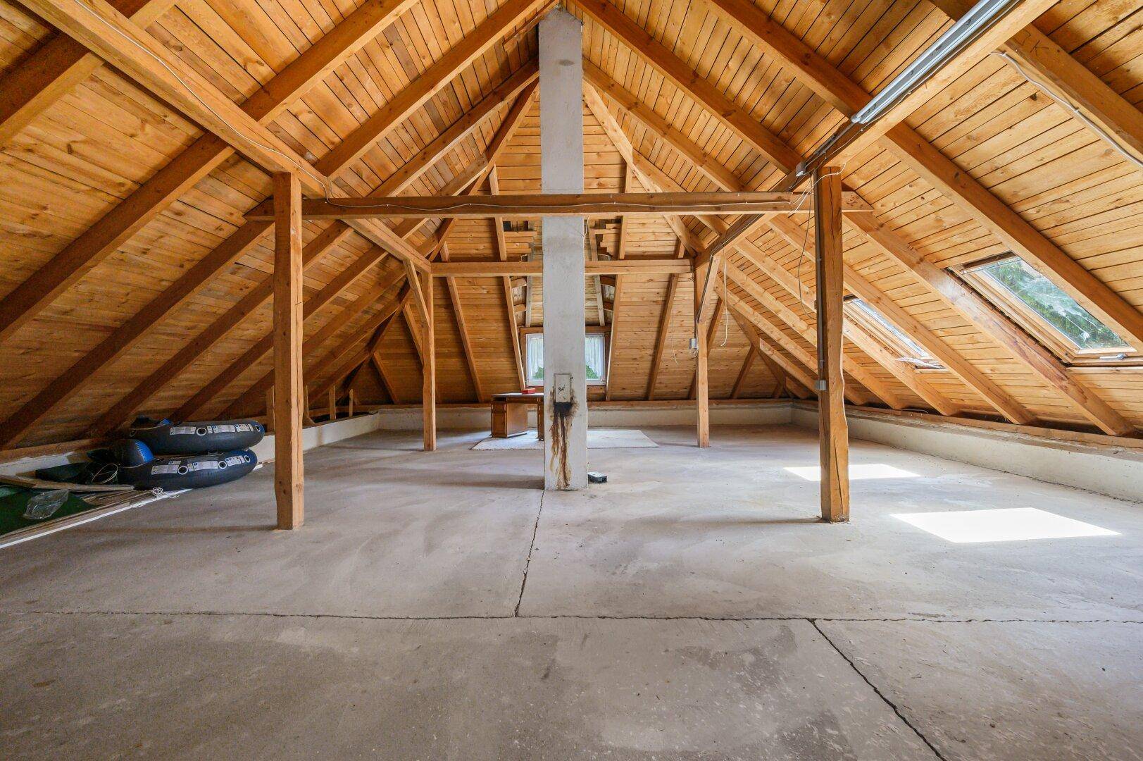 Geräumiger Dachboden mit sichtbaren Holzbalken und Dachfenstern, ideal für Ausbau.